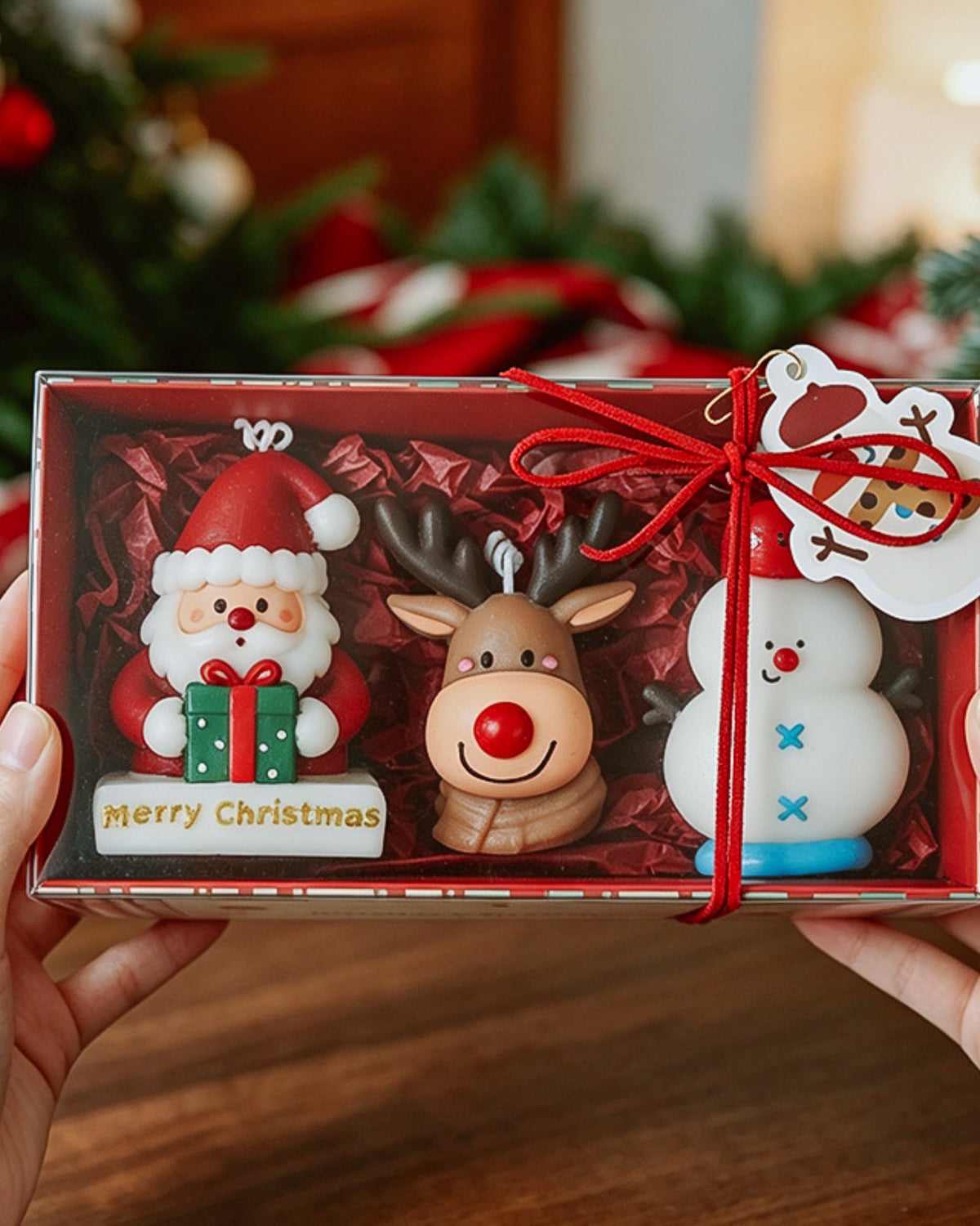 Hands holding a Santa, reindeer and snowman candle gift box tied with red ribbon