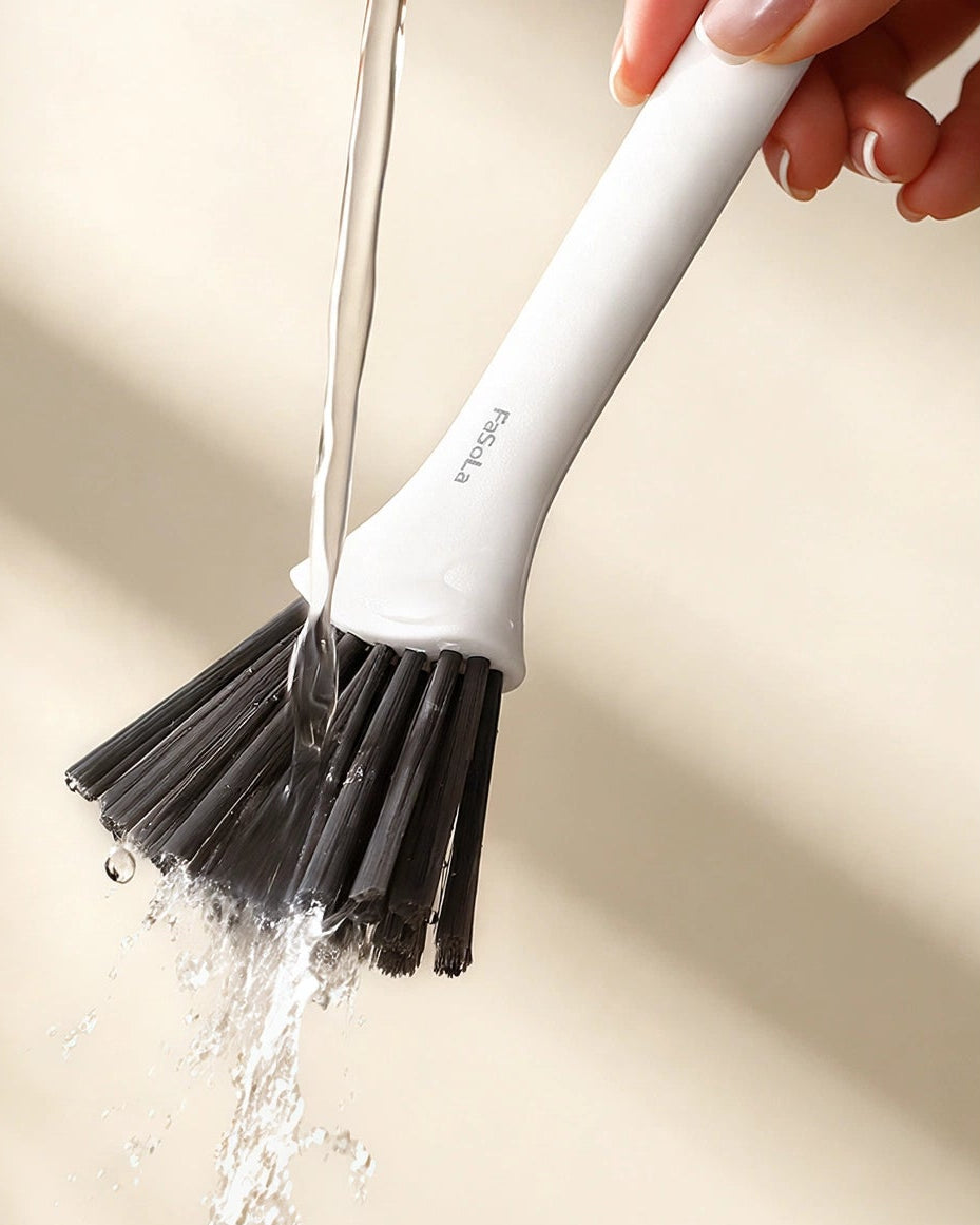 A hand holds a white and black cleaning brush under running water, with promotional text on the left reading 'Just Rinse With Water Clean As New'.