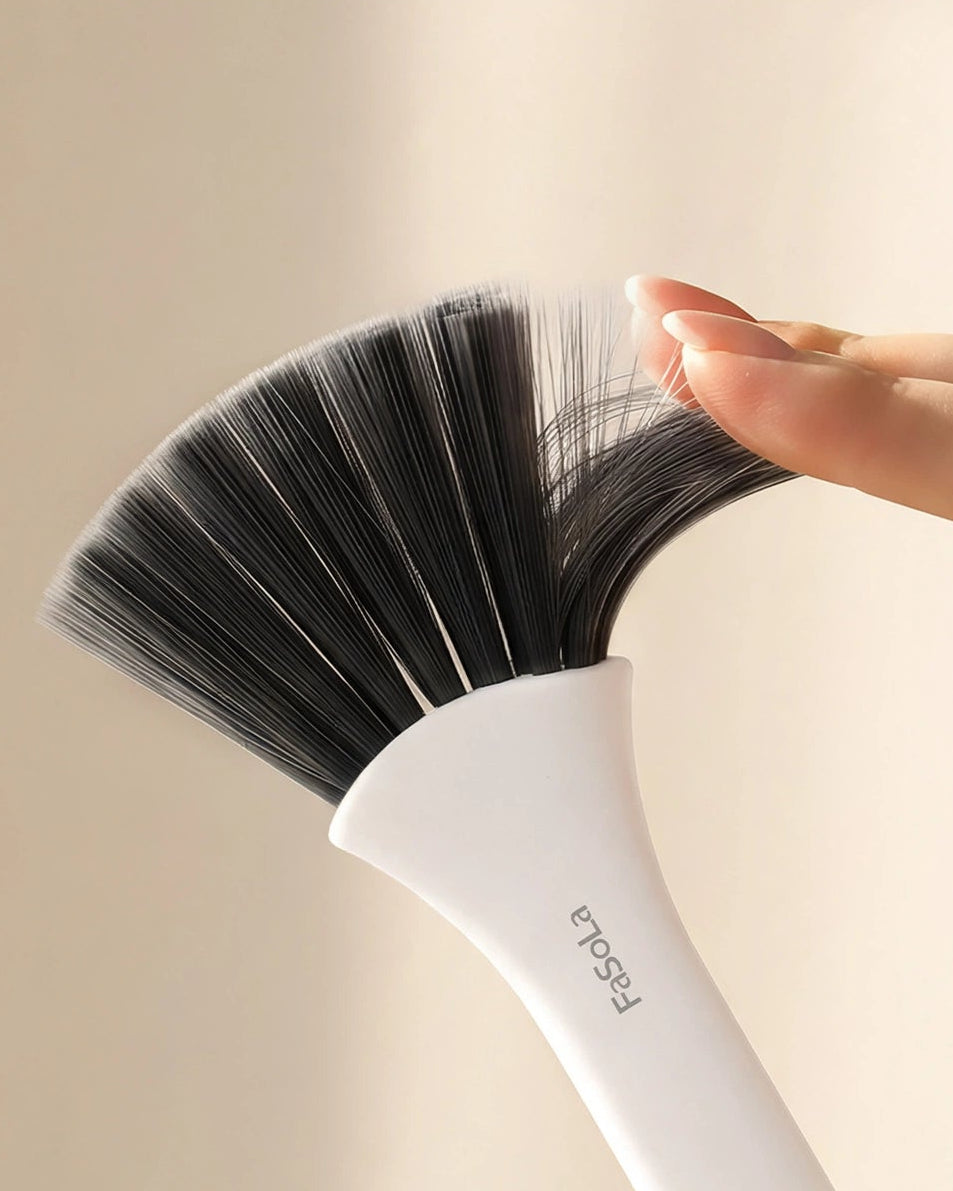 A soft, flexible-bristled makeup brush with a white handle and black bristles, shown with a hand touching the bristles to demonstrate gentleness. Text at the top reads 'Soft, Flexible Bristles Gentle On Surfaces'.