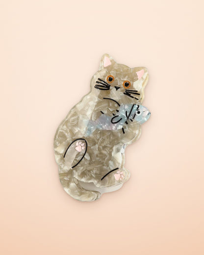 Kitten hugging a fish acetate claw clip on an apricot background