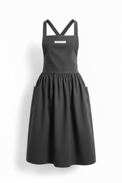 A dark gray sleeveless apron-style dress with a gathered waist, flared skirt, and crossed shoulder straps, shown on a plain white background.