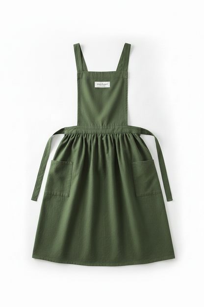 An olive green cotton apron with adjustable shoulder straps, a gathered waist, two front patch pockets, and a tie belt, shown flat on a white background.