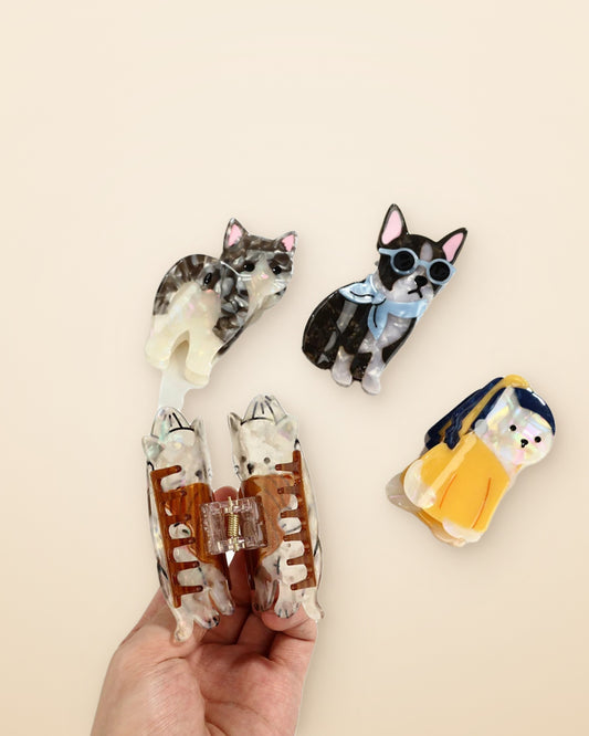 Hand holding cat and dog acetate claw clips on a sand background