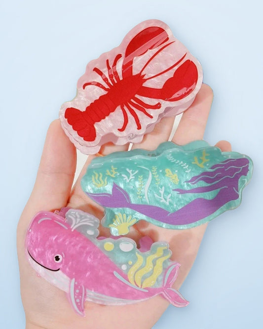 Hand holding lobster, mermaid and whale acetate claw clips on a sky blue background