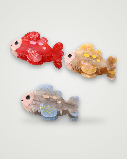Spotted fish acetate claw clips in Cherry Polka, Honey Glitter and Misty Blue on a light gray backdrop